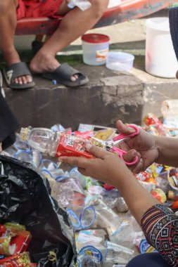 Bandung, Endonezya 29 Nisan 2025, plastik tasnif ve temizlik sırasında kırmızı plastik şişe etiketi kesen kadın.