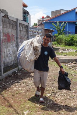Bandung, Endonezya 29 Nisan 2025, Kentin arka sokaklarında ağır çuval ve plastik torba taşıyan adam,