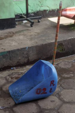 Bandung, Endonezya 29 Nisan 2025, uzun saplı mavi plastik faraş beton basamağın yanındaki ıslak zeminde dinleniyor.