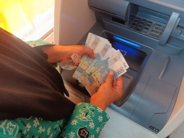 Bandung, Endonezya - 09 Mayıs 2025: Endonezya para transferi ve finans kullanımı için Endonezya rupiah banknotları kullanarak ATM makinesinden para çeken kadın
