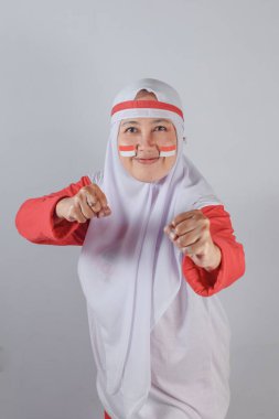 Beyaz tesettürlü Endonezyalı Müslüman kadın ve vatansever yüz boyası ile boks yaparken yumruklarını sıkarak harekete geçmeye hazır olduğunu gösteren kırmızı elbiseli kadın.