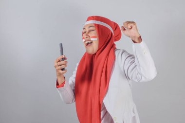 Tesettürlü Müslüman kadın Endonezyalı yüz boyası ile akıllı telefon kullanırken içeride neşe ve bağlantı kuruyor.