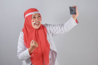 Müslüman kadın selfie çekerken sıkılmış bir yumruk ve vatansever yüz boyasıyla gülümsüyor, bağımsızlığı heyecan ve gururla kutluyor.