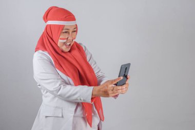 Yüzü boyalı Endonezyalı Müslüman kadın akıllı telefonuyla selfie çekerken bağımsızlık ve dijital ifadeyi kutlamak için gülümsüyor ve gülüyordu.
