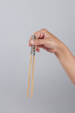 El dikey olarak bambu yemek çubuklarını tutuyor ve çiçek saplarıyla sade gri zemin üzerinde duruyor.