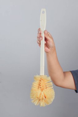 Tuvalet fırçası dikey olarak üst kulptan tutulmuş ve sarı kıllar aşağıya bakıyor.