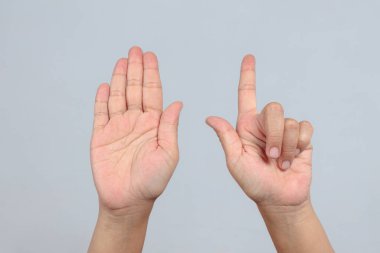 İki el açık avuç içiyle yedi numarayı oluşturur ve gri arka planda işaret diliyle parmak kaldırır. Sayma hareketi ve sözsüz iletişimi sembolize eder.