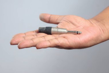 Erkek el, çeyrek inç ses kablosu konnektörünü açık avuçta tutuyor. Tarafsız arka planda, teknolojik bakım ve bağlantı kavramına sahip elektronik aksesuar detaylarını gösteriyor.
