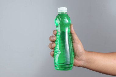 El ele tutuşan yeşil plastik şişe, gri kapaklı.