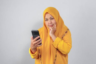 Tesettürlü düşünceli kadın telefonunu kontrol ederken düşünüyor.