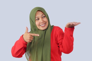 Neşeli tesettürlü kadın avucunu açarken gülümsüyor, ürün konseptini tanıtıyor veya sunuyor, izole edilmiş stüdyo çekimi, reklam görselleri için mükemmel.