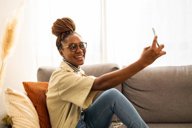 Gülümseyen genç Afrikalı Amerikalı kadın cep telefonu evde selfie çekmek için. . 