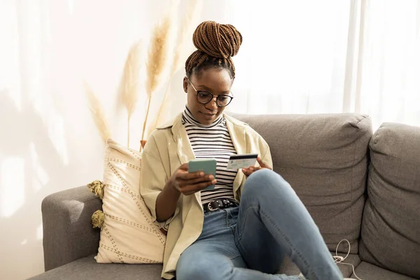 Young African American woman mobile phone tablet at home . She is doing digital banking, shopping online.