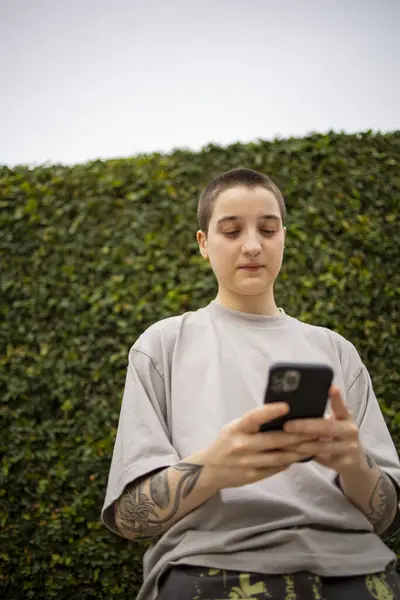Portrait of Latin transgender generation z person using mobile phone. He is making selfie and text messaging outdoors