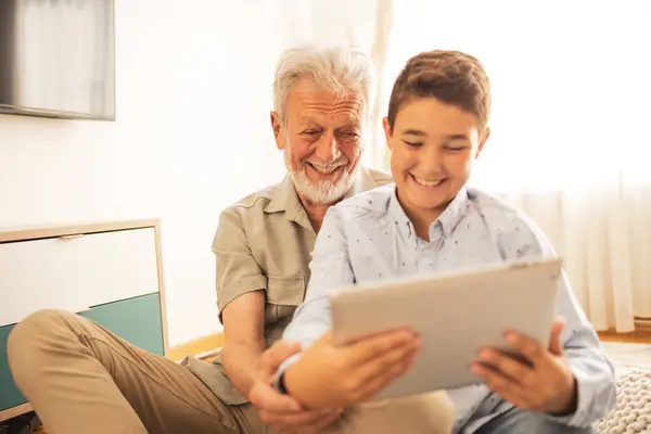 Smiling cute grandson teaching grandfather to use digital tablet at home during weekend