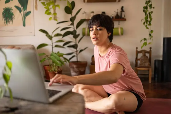 stock image Young latin girl with a short hair using a laptop. She is sitting in the room full of green plants wearing a pink shirt. High quality photo