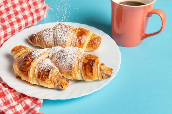 Delicious croissants filled with chocolate and sprinkled with fine sugar with a cup of coffee on a colorful background and a checkered tablecloth. High quality photo