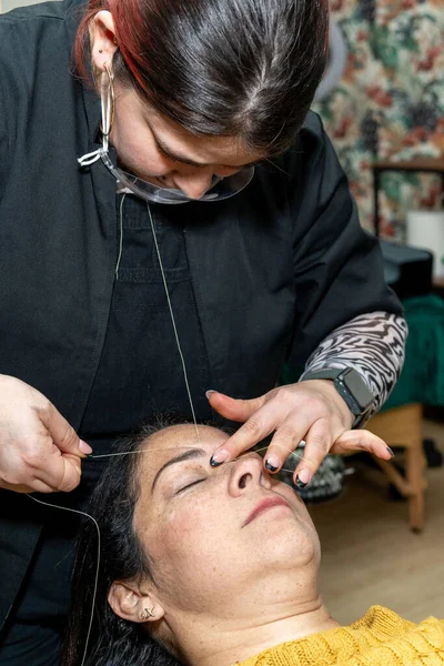 Makeup and eyebrow artist performs threading for client in beauty salon. High quality photo