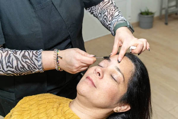 Brow and make up artist shaping and coloring eyebrows of her woman client in salon. Procedure in process.