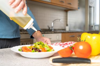 Evdeki mutfakta taze domates, marul ve havuç salatasına zeytinyağı koyan kadına yakın çekim. Sağlıklı ve yemek konsepti yapmak kolay. Yüksek kalite fotoğraf