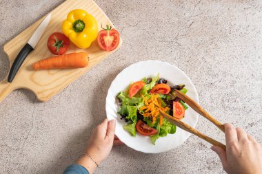 Kadın elinin yukarıdan görünüşü taş masanın üzerinde ahşap maşayla lezzetli taze salata topluyor. Sağlıklı gıda konsepti. - Evet. Yüksek kalite fotoğraf
