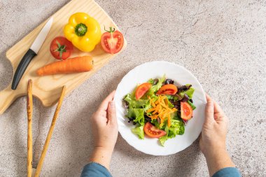 Tahta bir tahtanın üzerinde çeşitli sebzelerle lezzetli ve taze bir tabak salata tutan kadınların ellerinden manzara. Sağlıklı gıda konsepti. - Evet. Yüksek kalite fotoğraf
