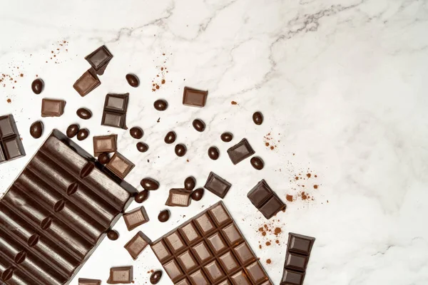 View from above of dark and milk chocolate bars and various pieces cut out on marble top. High quality photo
