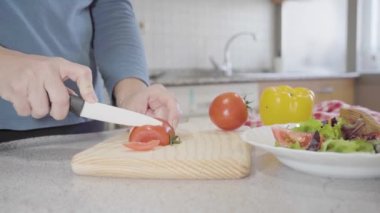 Kadın salata hazırlamak için mutfaktaki ahşap bir tahtada domates kesiyor. Sağlıklı ve lezzetli yemek konsepti. Yüksek kalite fotoğraf