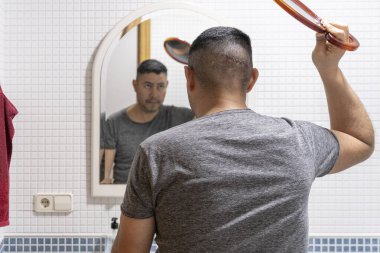 A man, after fainting, examines his head wound with staples using bathroom mirror and handheld mirror clipart
