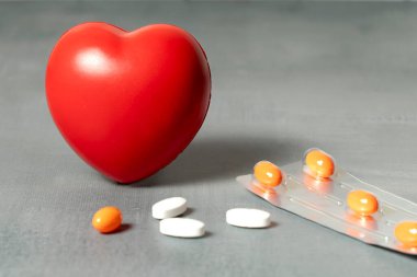 Dağınık hapların yanına yerleştirilmiş kırmızı bir kalp stres topu ve turuncu bir hap..
