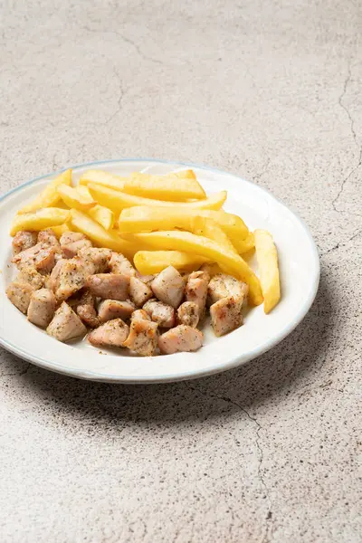Beyaz tabakta patates kızartması ve leziz domuz eti servisi. Basit ama tatmin edici bir yemeği temsil ediyor.