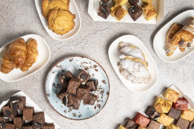 Tabaklara ve kutulara yerleştirilmiş çeşitli hamur işleri ve brovnilerin genel görüntüsü yemek fotoğrafçılığı için cazip bir daire oluşturuyor.