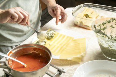 Makarna tabakalarını ricotta ve ıspanak karışımıyla dolduran eller.