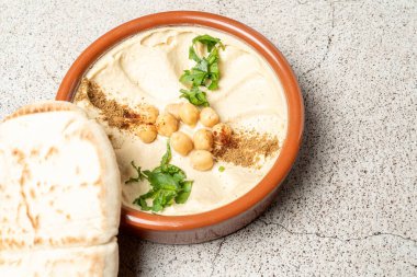 Nohut, baharat ve otlarla kaplı kremalı humus terakotta kasesinde pide ekmeği ile servis edilerek, canlı ve lezzetli bir orta doğu mutfağı deneyimi sunuluyor.