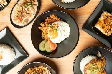 Ahşap bir masada servis edilen çeşitli Asya yemeklerinin genel görünümü, Asya mutfağının çeşitliliğini gözler önüne seriyor.