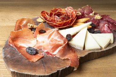 Dilimlenmiş İber jambonu, sucuk, peynir, fındık ve kuru üzümler ahşap bir tabakta dizilmiş, baştan çıkarıcı bir aperatif ya da aperatif oluşturur.