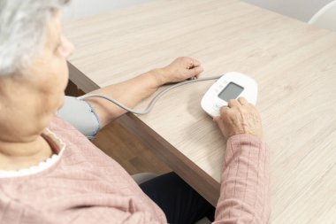 Dijital gerilim ölçer kullanan yaşlı bir kadın, evde tansiyon ölçümü yapıyor.