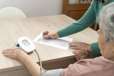 Hemşire, yaşlı bir kadının tansiyonunu ölçerken tansiyon ölçer.