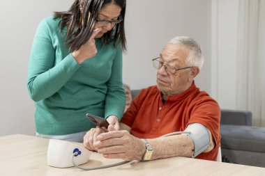 Kızı, babasının kan basıncını evde dikkatlice ölçüyor, ona destek oluyor ve sağIığını koruyor.