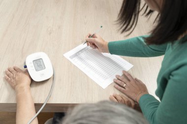 Hemşire, bir sağlık raporuna tansiyon ölçer kullanarak kan basıncını ölçüyor.