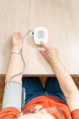 Tansiyonunu ölçmek için dijital gerilim ölçer kullanan yaşlı bir adam, evde sağlık denetimini destekliyor