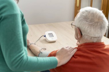 Hemşire, tansiyon ölçer kullanan yaşlı bir adamın tansiyonunu ölçüyor, sağlık hizmeti veriyor ve hayati belirtileri izliyor.