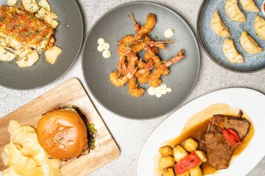 Ekmekli karides, burger ve kızarmış et içeren uluslararası yemekler tabakta sergileniyor.