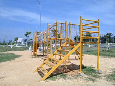 Güneşli bir günde oyun parkı ekipmanları. Çimenli bir alanda slaytlı ve tırmanma çubukları olan sarı metal oyun alanı yapısı.