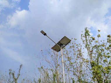 Güneş enerjili sokak lambası beyaz bulutlu mavi gökyüzüne karşı. Açık alanlar için sürdürülebilir ışıklandırma çözümü.