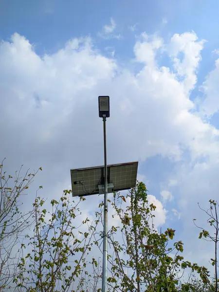 Güneş enerjili sokak lambası beyaz bulutlu mavi gökyüzüne karşı. Açık alanlar için sürdürülebilir ışıklandırma çözümü.