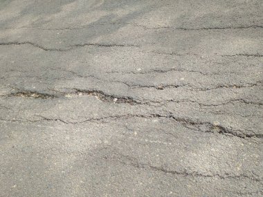 Çatlamış ve yıpranmış asfalt yol yüzeyinde görünür çukurlar ve küçük taşlar var..