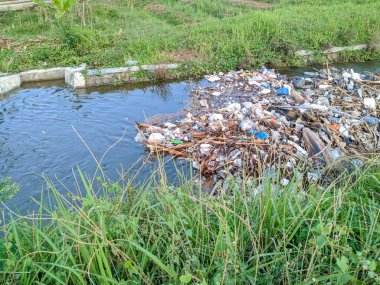 Kirlenmiş bir su yolu plastik torbalar, şişeler ve diğer döküntülerle tıkanmış..