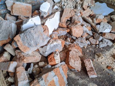 Kırık tuğla yığınları ve beton döküntüleri inşaat alanını kirletti. Toz ve enkaz görülebiliyor, bu da yıkımı gösteriyor..