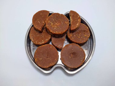 Round slices of dark brown palm sugar rest on a silver platter against a white background. The sugar has a slightly sticky texture and is slightly misshapen. clipart